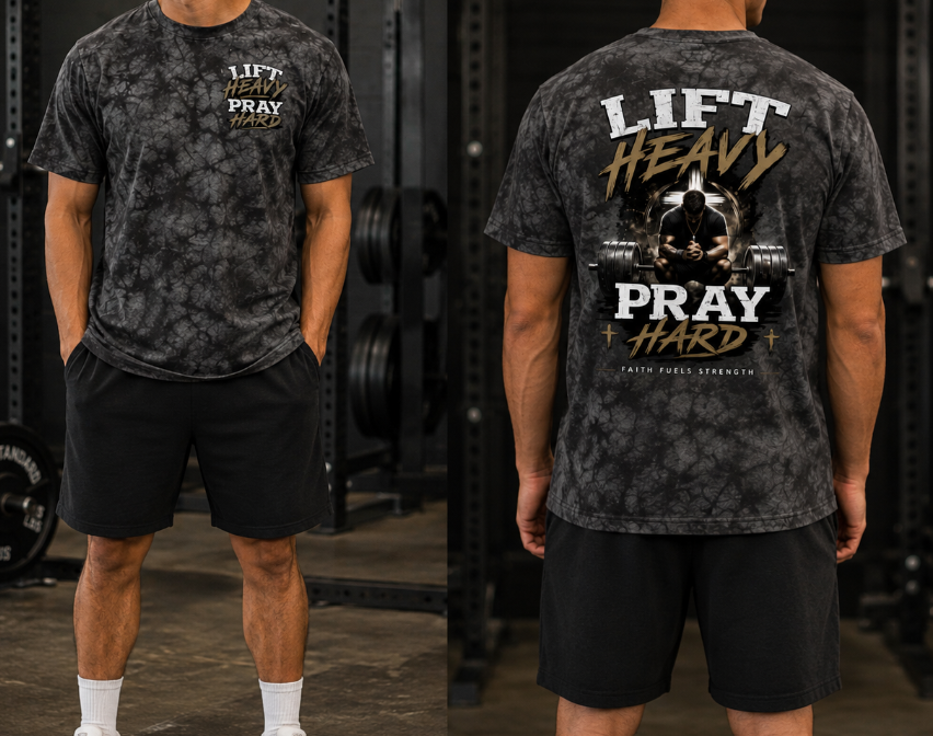 A man modeling a dark gray acid-wash graphic t-shirt in a gym setting, shown from both the front and back. The front features a small white and gold graphic reading 'LIFT HEAVY PRAY HARD'.